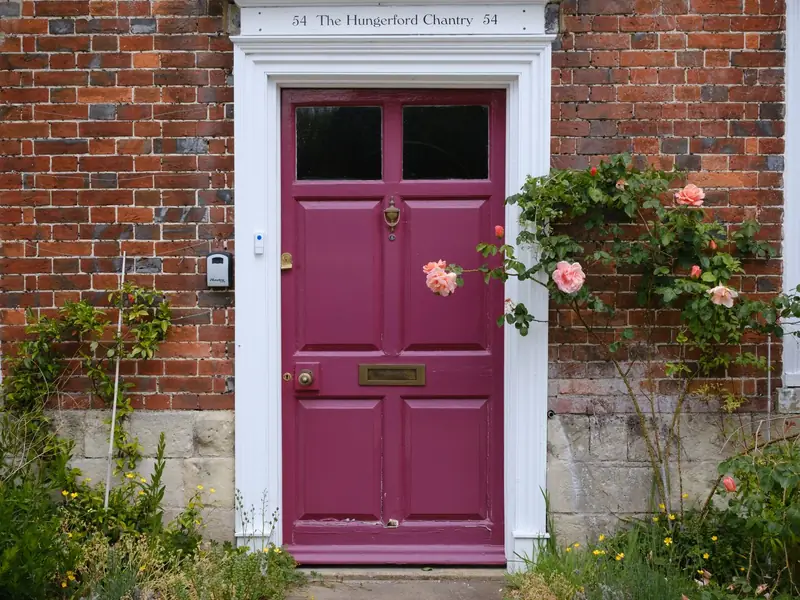 Deep pink door with climbing roses set in a brick wall, Hungerford, England